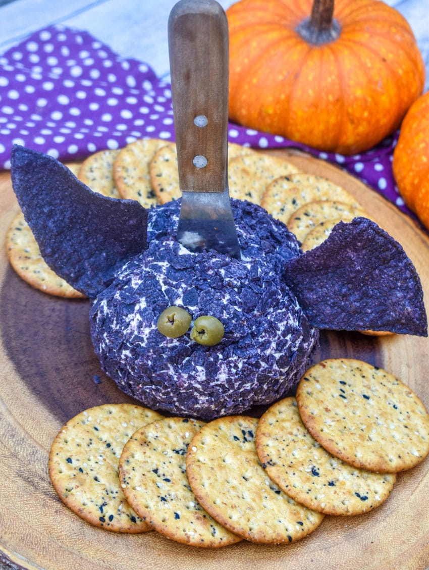 a halloween themed bat cheese ball surrounded by crackers on a wooden serving board