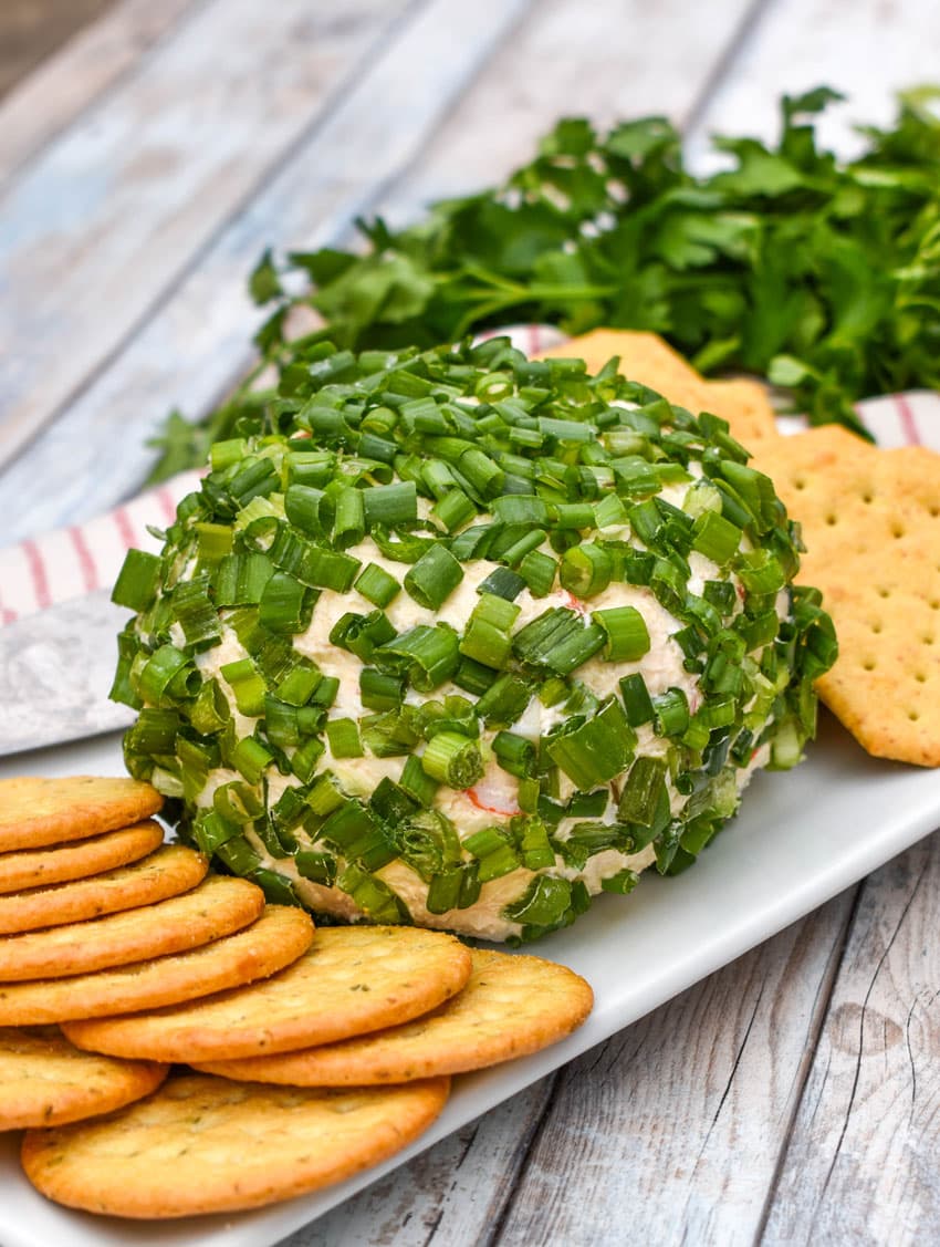 a green onion coated crab rangoon cheese ball surrounded by crackers on a white serving platter