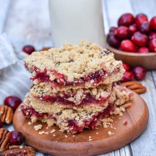 a stack of cranberry crumble bars on a small wooden serving board