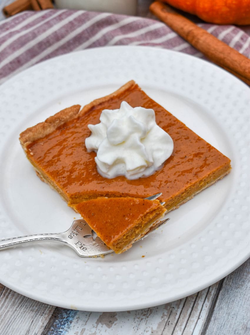 a slice of pumpkin slab pie topped with whipped cream on a small white plate
