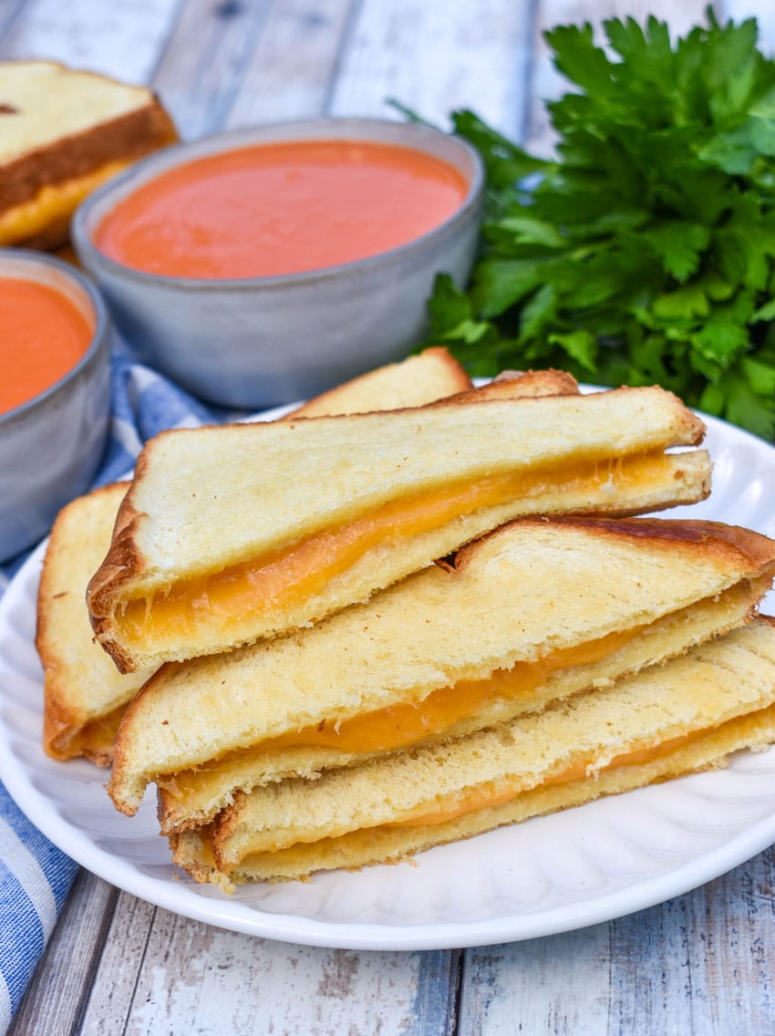 slices of sheet pan grilled cheese on a white plate with a small bowl of tomato soup on the side