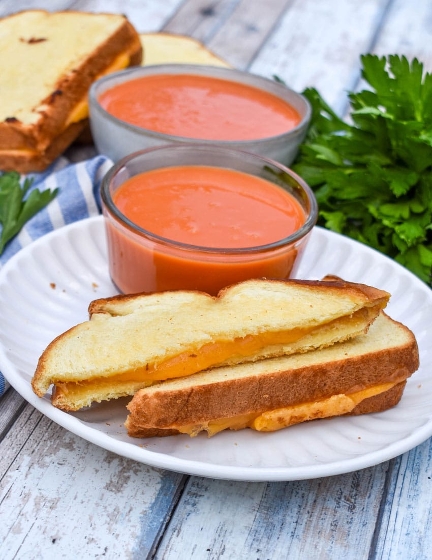 slices of sheet pan grilled cheese on a white plate with a small bowl of tomato soup on the side