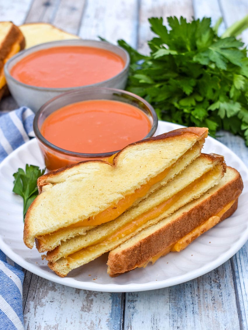 slices of sheet pan grilled cheese on a white plate with a small bowl of tomato soup on the side