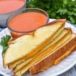 slices of sheet pan grilled cheese on a white plate with a small bowl of tomato soup on the side