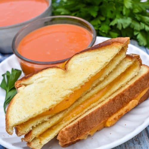 slices of sheet pan grilled cheese on a white plate with a small bowl of tomato soup on the side