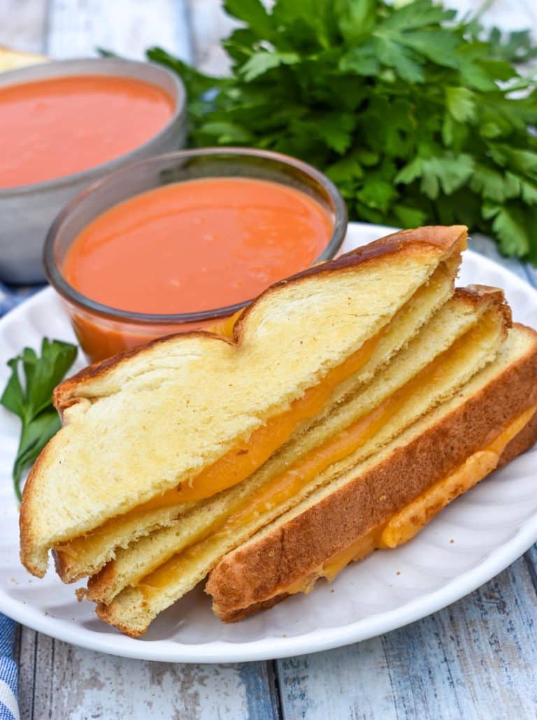 slices of sheet pan grilled cheese on a white plate with a small bowl of tomato soup on the side