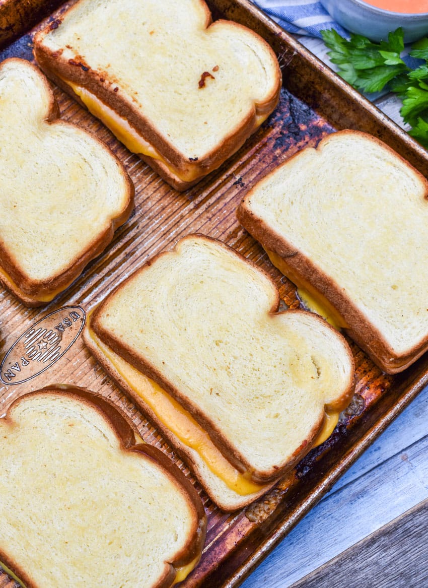 grilled cheese sandwiches arranged in two rows on a metal baking sheet pan