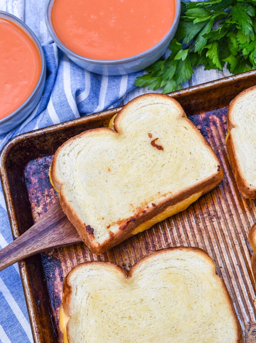 a wooden spatula lifting a grilled cheese sandwich off a rimmed sheet pan