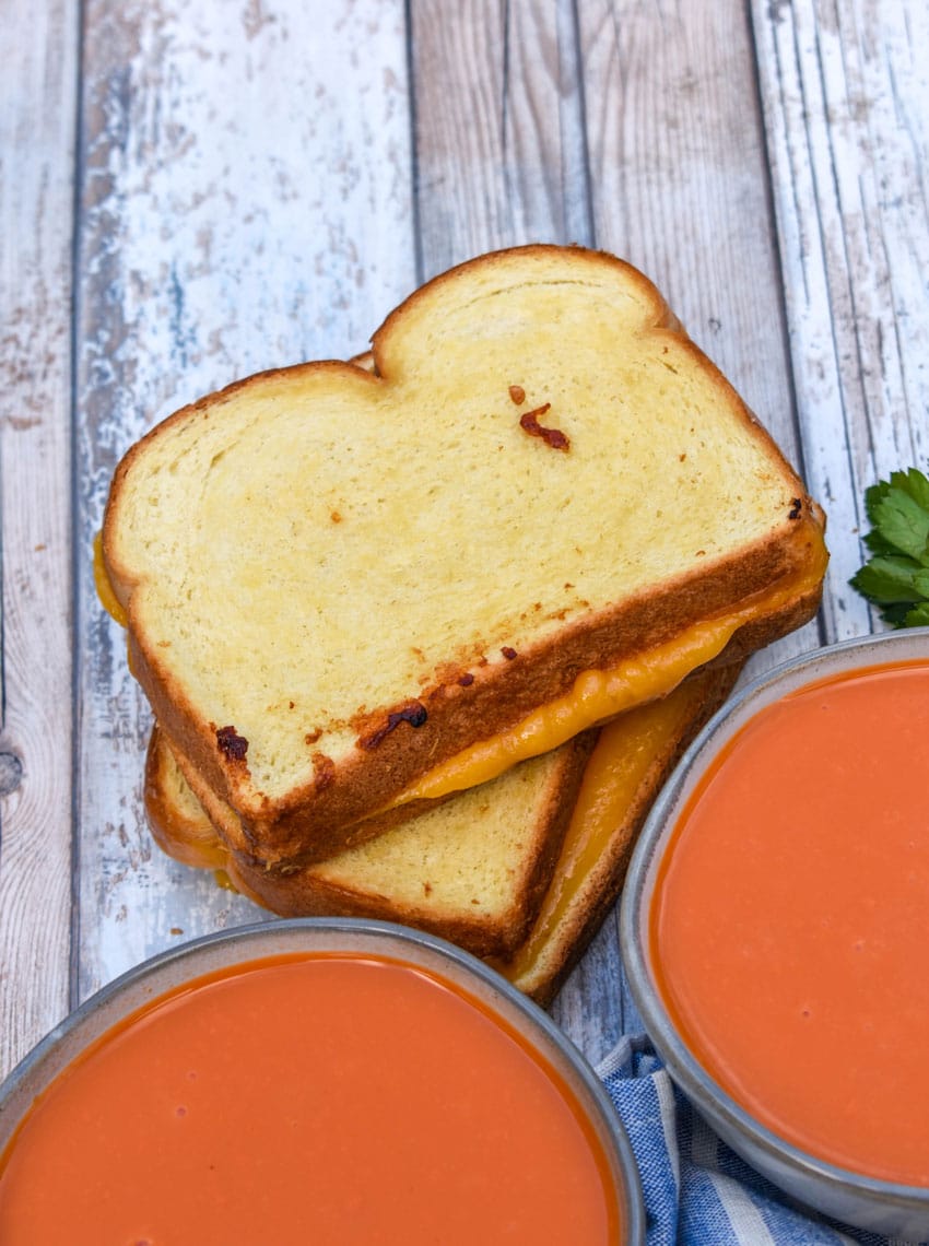 two sheet pan grilled cheese sandwiches stacked next to two small bowls of tomato soup