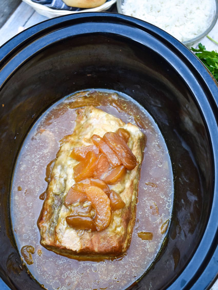 a slow cooked apple pie pork loin in juices in the black bowl of a crockpot