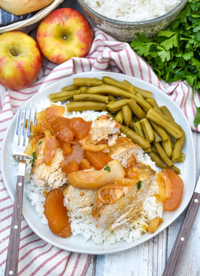slices of slow cooked apple pie pork loin over steamed white rice on a white plate