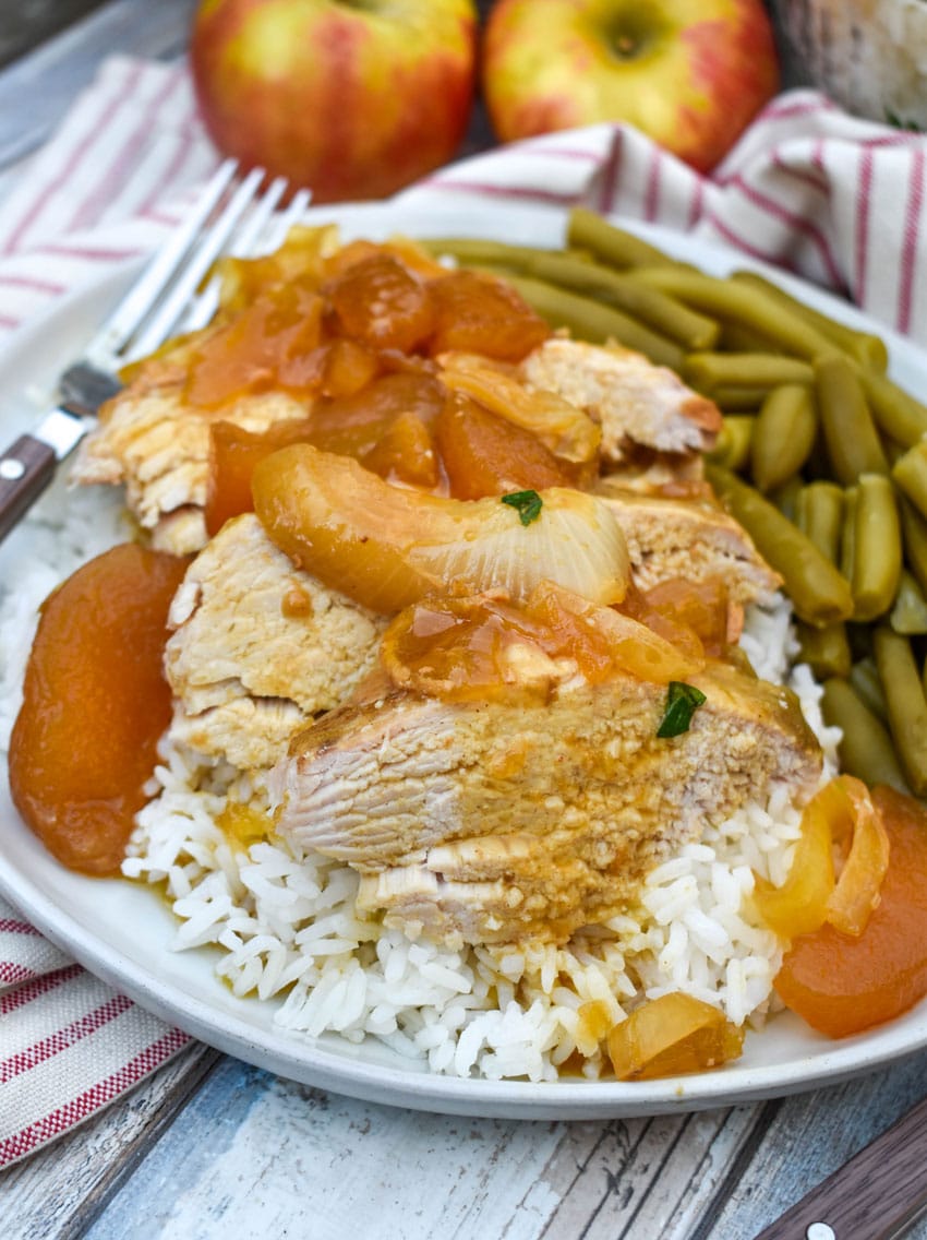 slices of slow cooked apple pie pork loin over steamed white rice on a white plate