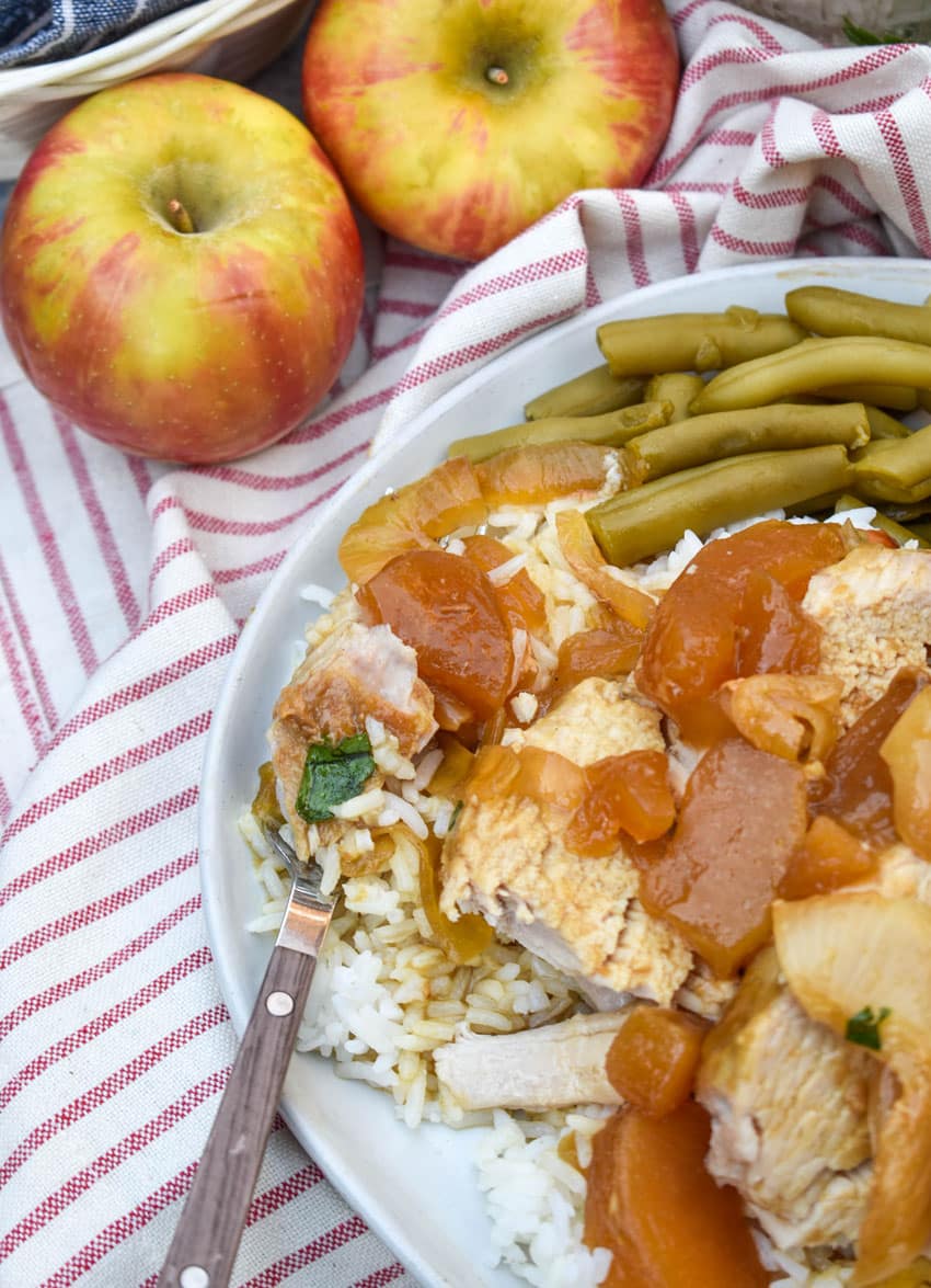 slices of slow cooked apple pie pork loin over steamed white rice on a white plate