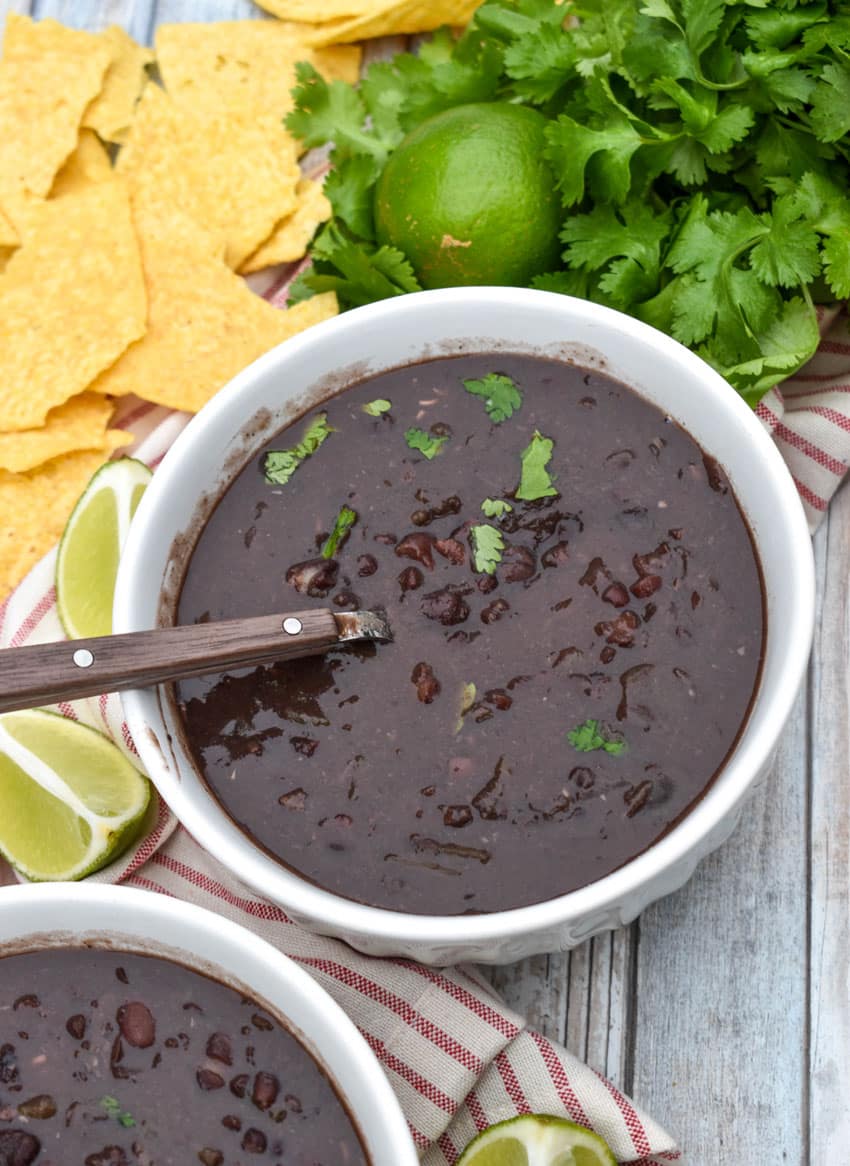 slow cooker black bean soup topped with fresh cilantro in two white bowls with lime wedges on the side