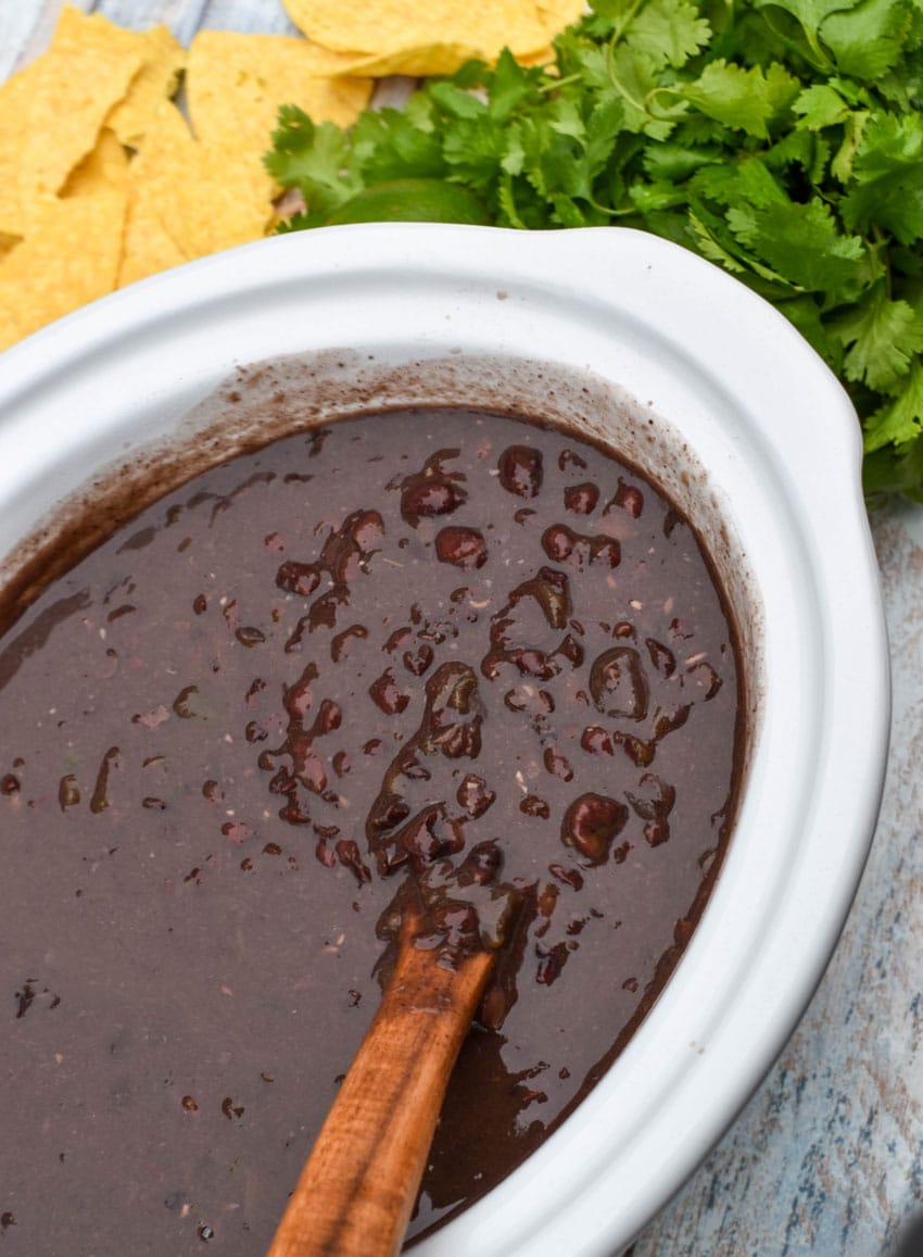 a wooden ladle scooping homemade black bean soup out of the white bowl of a slow cooker