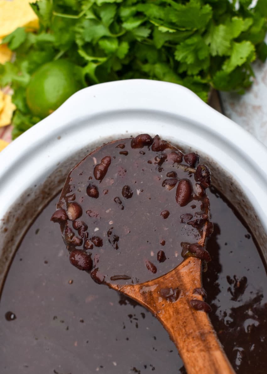 a wooden ladle scooping homemade black bean soup out of the white bowl of a slow cooker