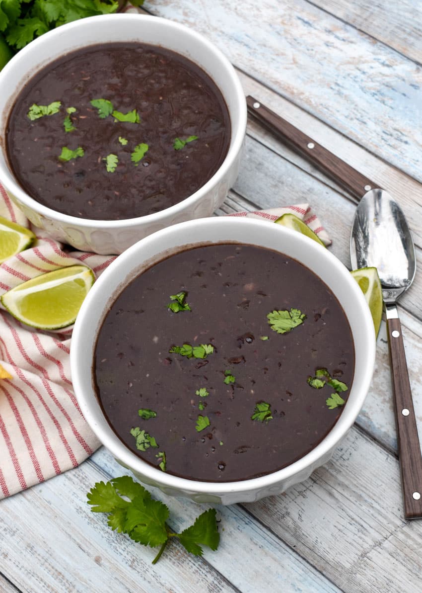 slow cooker black bean soup topped with fresh cilantro in two white bowls with lime wedges on the side