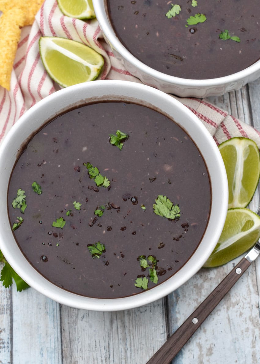 slow cooker black bean soup topped with fresh cilantro in two white bowls with lime wedges on the side