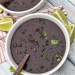 slow cooker black bean soup topped with fresh cilantro in two white bowls with lime wedges on the side
