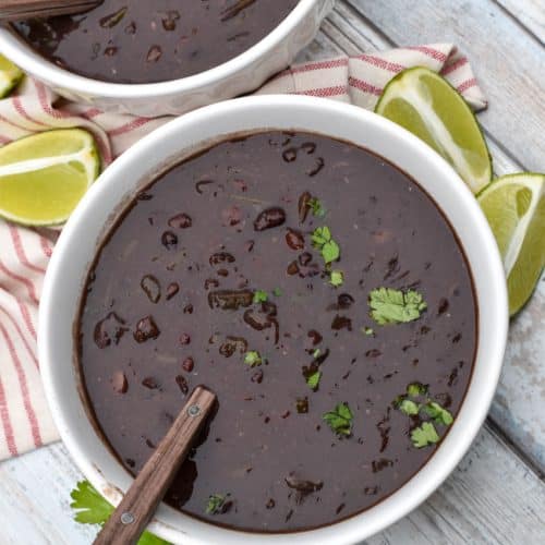 slow cooker black bean soup topped with fresh cilantro in two white bowls with lime wedges on the side