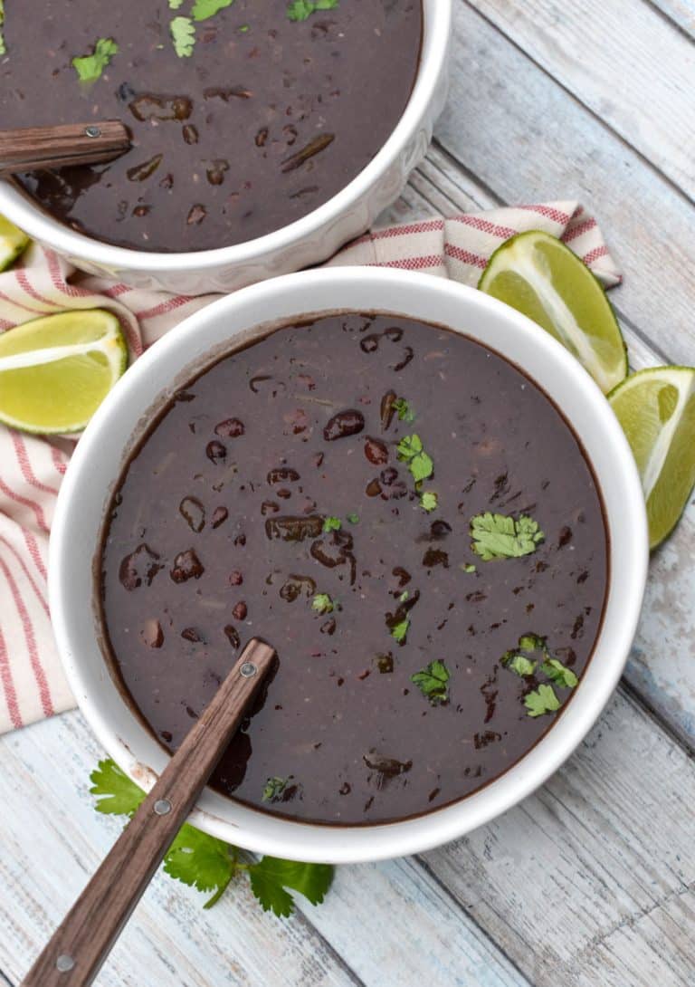 slow cooker black bean soup topped with fresh cilantro in two white bowls with lime wedges on the side