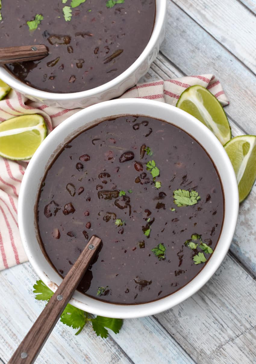 slow cooker black bean soup topped with fresh cilantro in two white bowls with lime wedges on the side