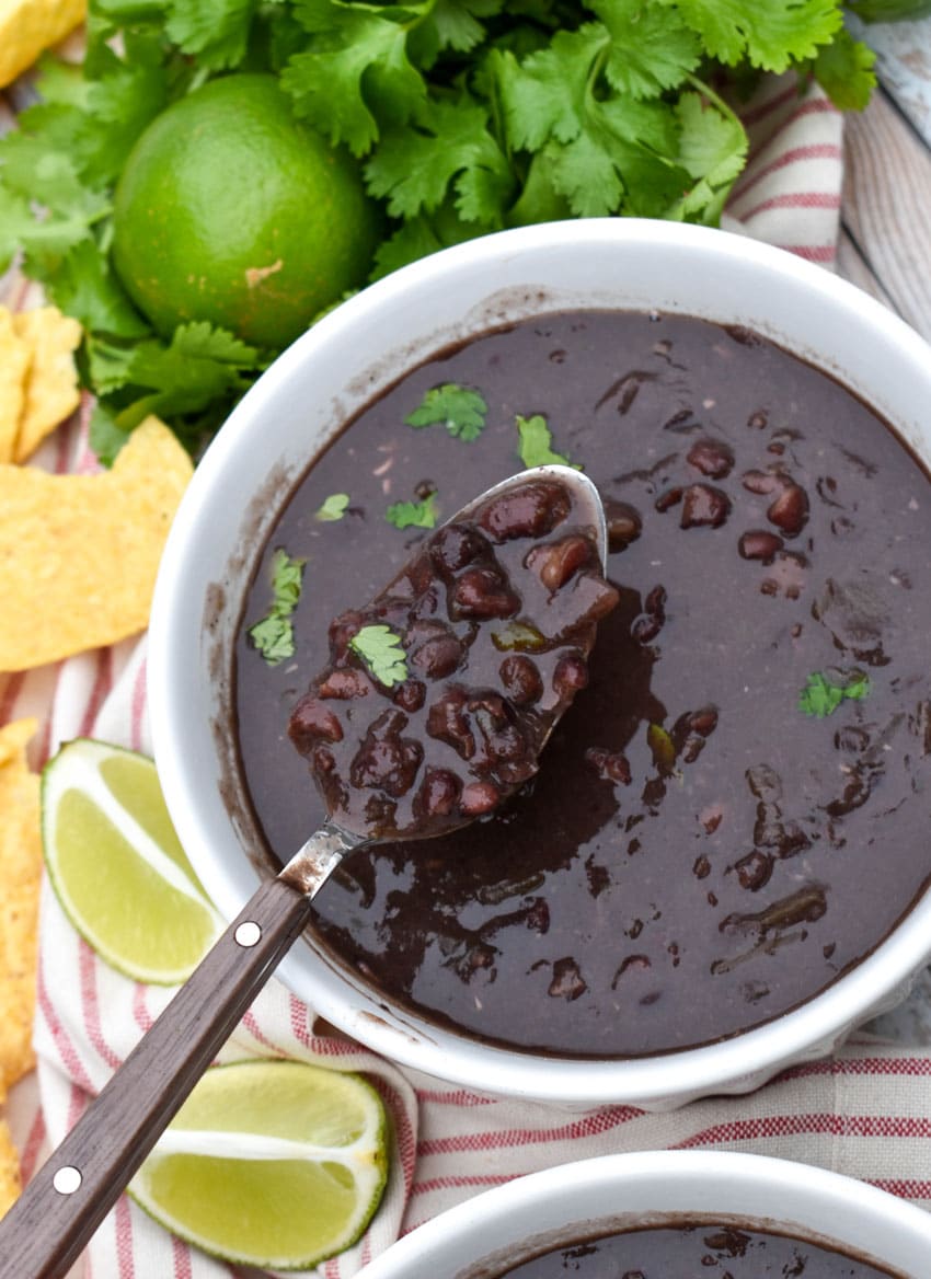 slow cooker black bean soup topped with fresh cilantro in two white bowls with lime wedges on the side