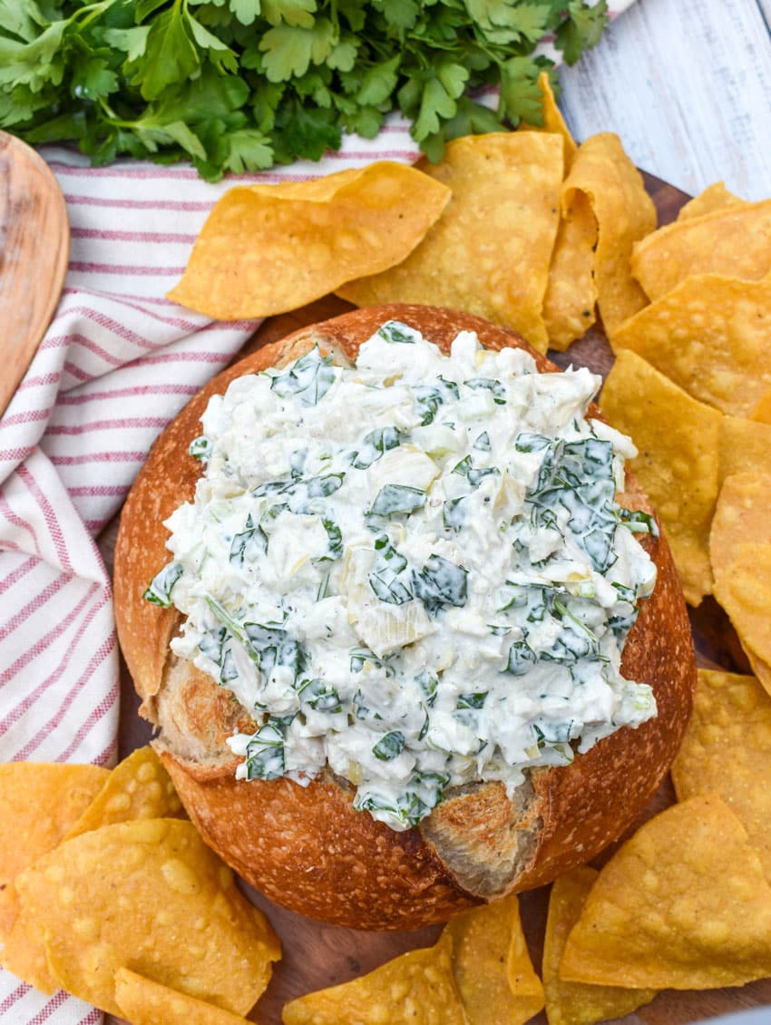 spinach artichoke chicken salad in a hollowed out bread bowl surrounded by tortilla chips