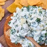 spinach artichoke chicken salad in a hollowed out bread bowl surrounded by tortilla chips