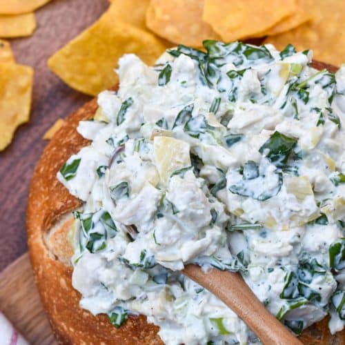 spinach artichoke chicken salad in a hollowed out bread bowl surrounded by tortilla chips