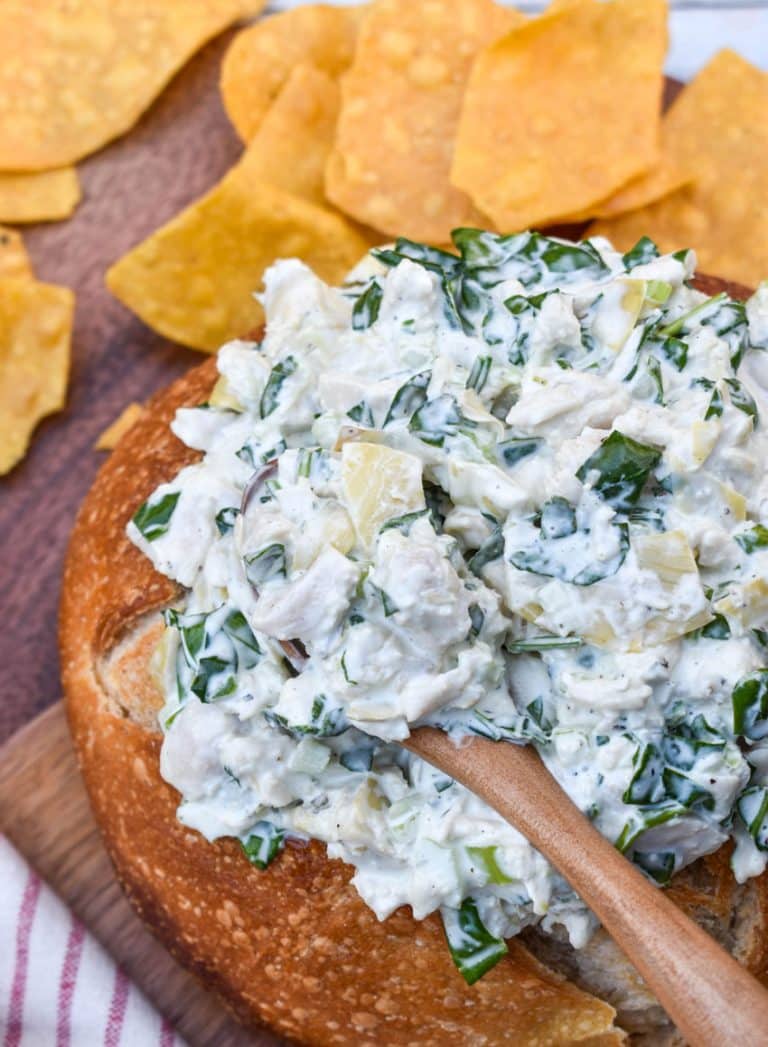 spinach artichoke chicken salad in a hollowed out bread bowl surrounded by tortilla chips