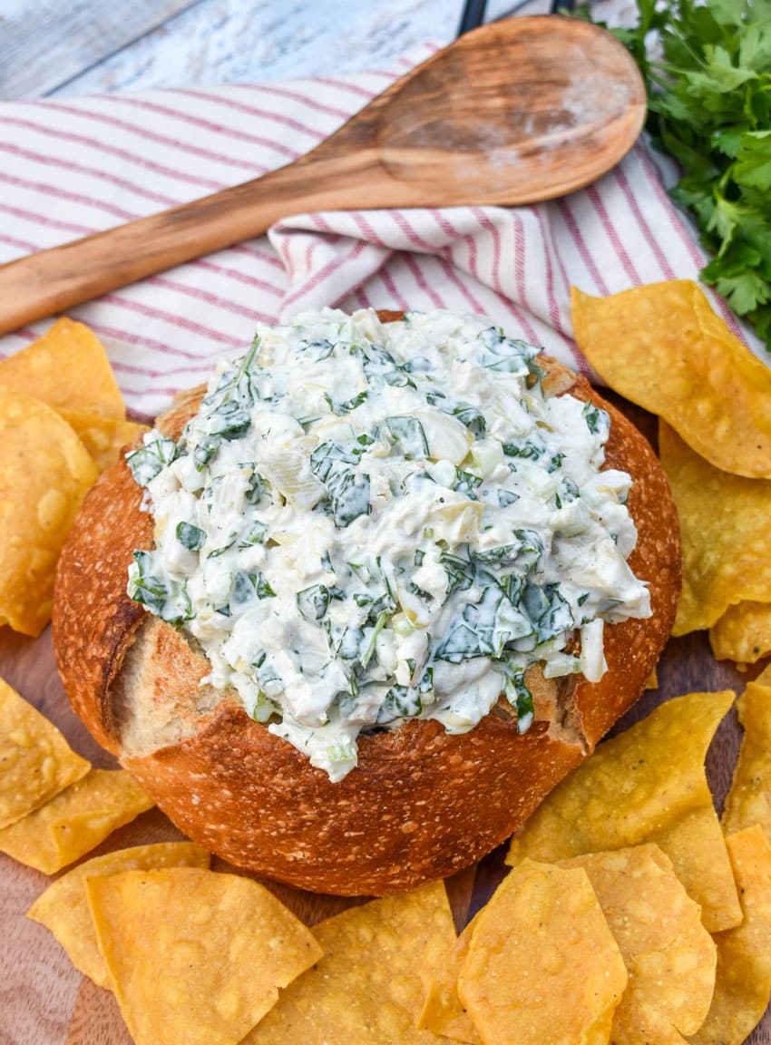 spinach artichoke chicken salad in a hollowed out bread bowl surrounded by tortilla chips