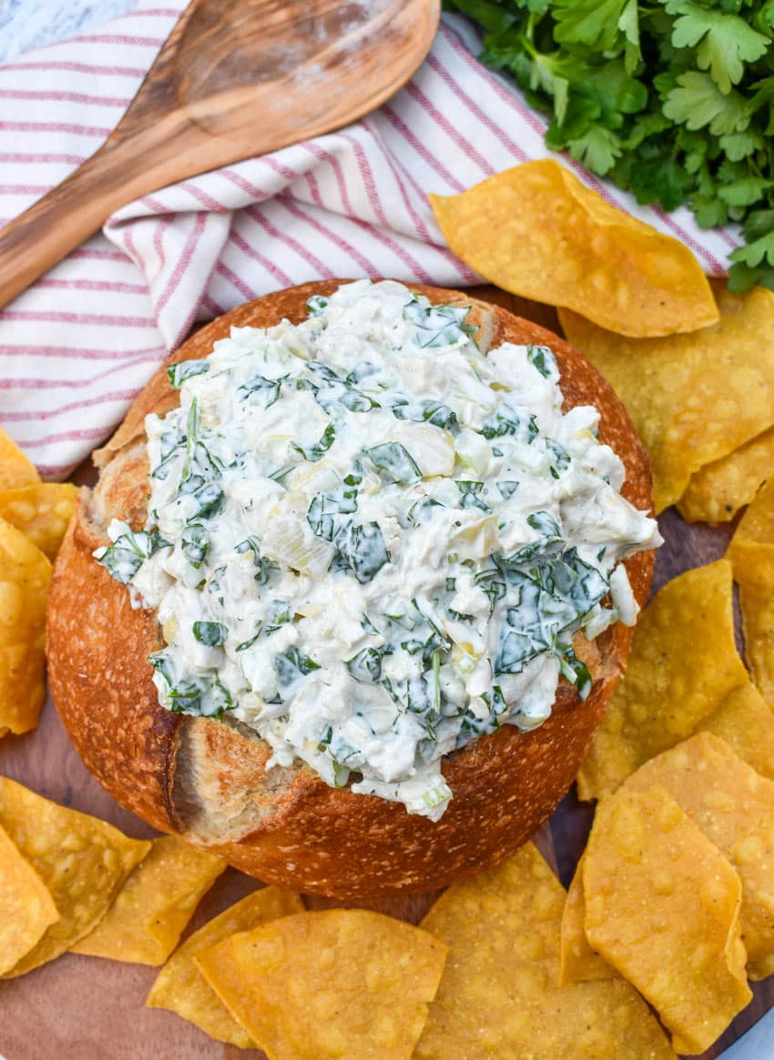 spinach artichoke chicken salad in a hollowed out bread bowl surrounded by tortilla chips