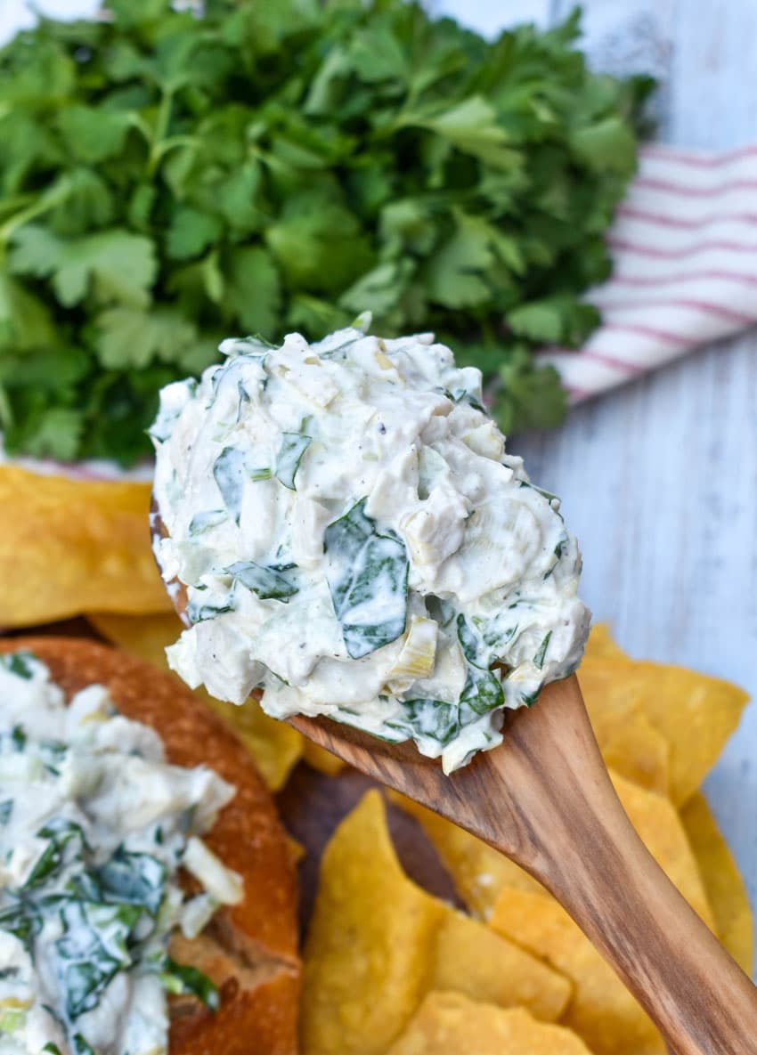 a wooden spoon holding up a scoop of spinach artichoke chicken salad