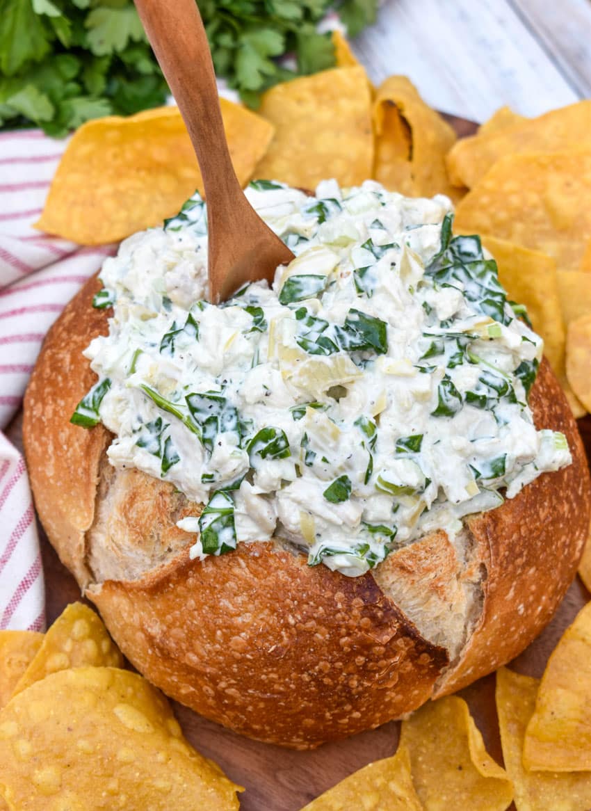 spinach artichoke chicken salad in a hollowed out bread bowl surrounded by tortilla chips