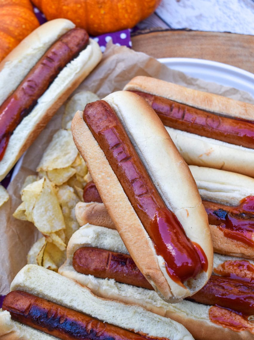 a stack of witch finger hotdogs with ketchup on a wooden serving tray