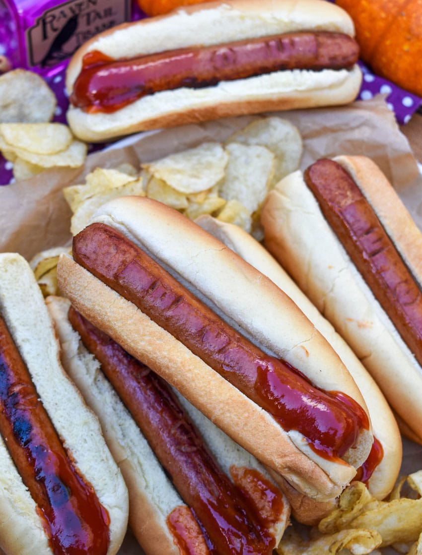 a stack of witch finger hotdogs with ketchup on a wooden serving tray