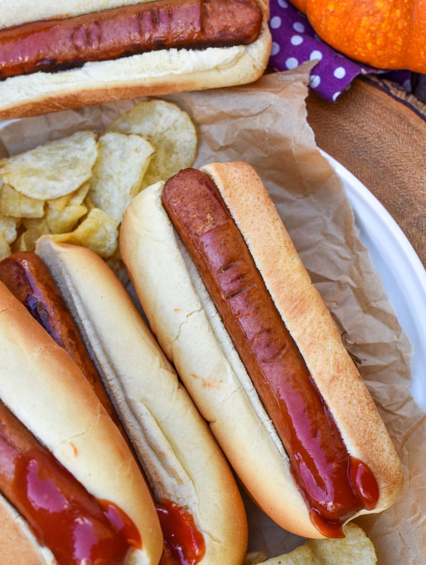 a stack of witch finger hotdogs with ketchup on a wooden serving tray