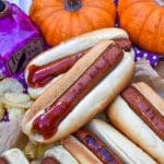 a stack of witch finger hotdogs with ketchup on a wooden serving tray