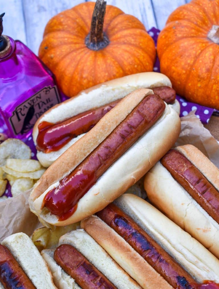 a stack of witch finger hotdogs with ketchup on a wooden serving tray