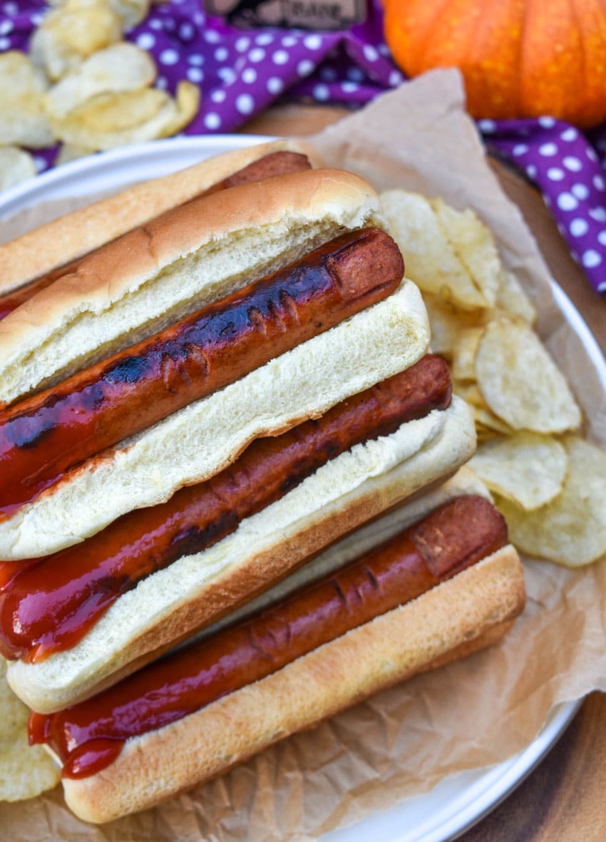 a stack of witch finger hotdogs with ketchup on a wooden serving tray