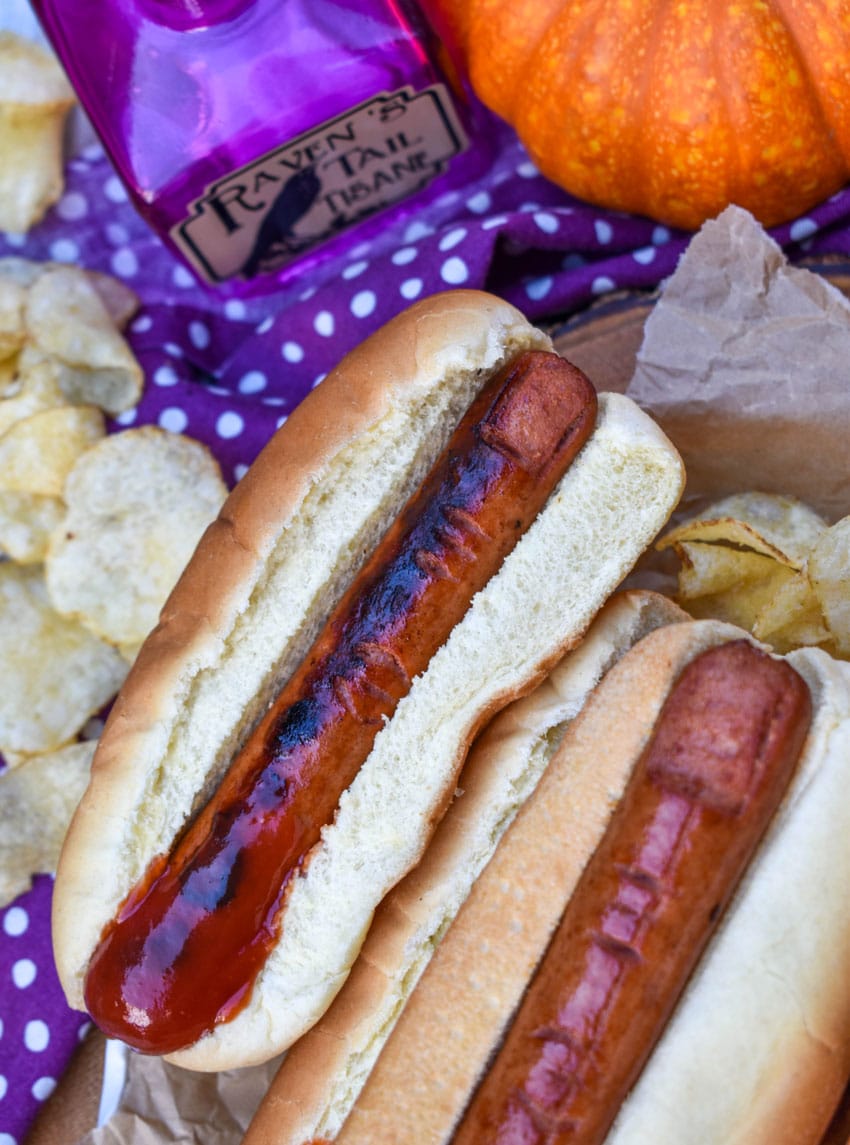 a stack of witch finger hotdogs with ketchup on a wooden serving tray
