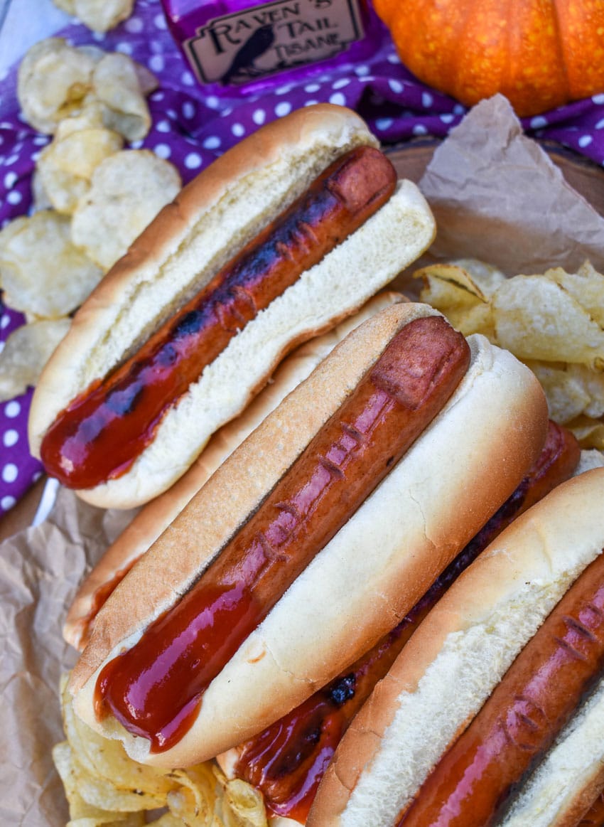 a stack of witch finger hotdogs with ketchup on a wooden serving tray