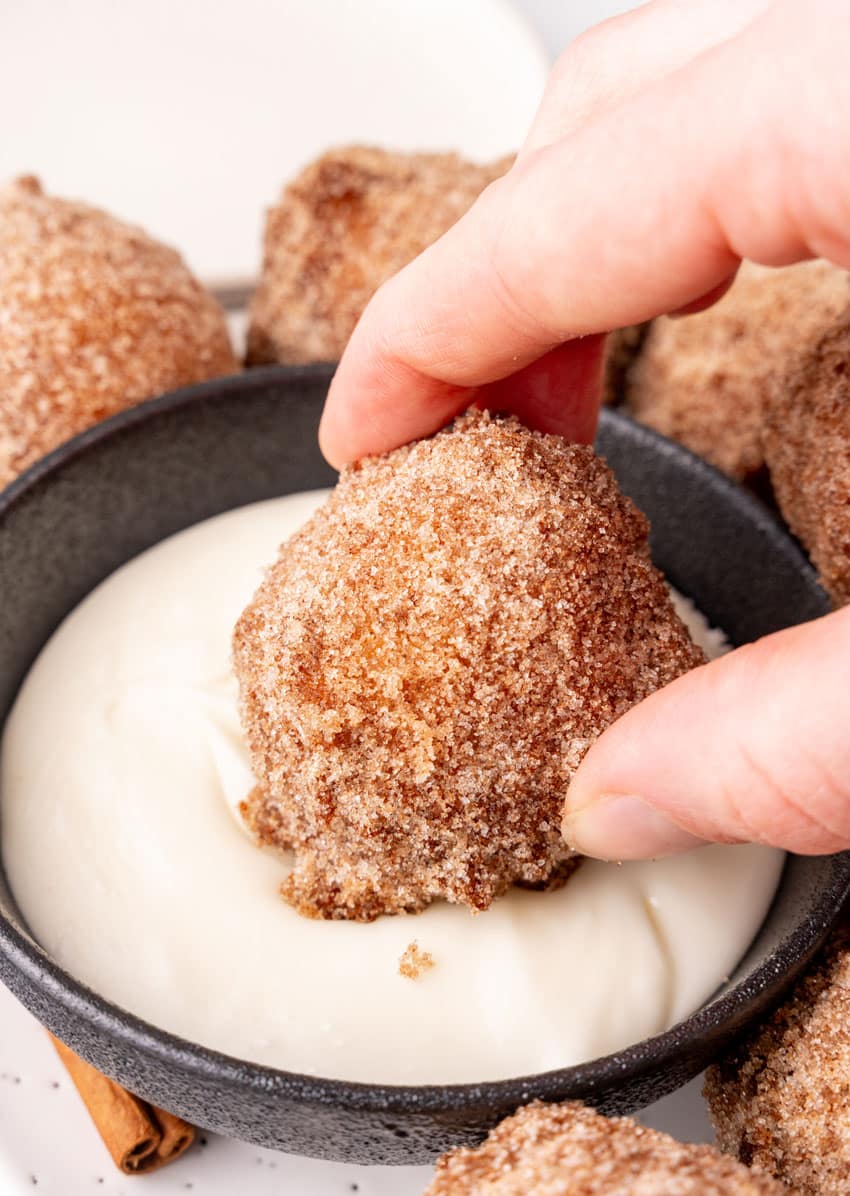 a hand dunking a homemade pancake puppy into a small bowl of thick sweet cream cheese dip