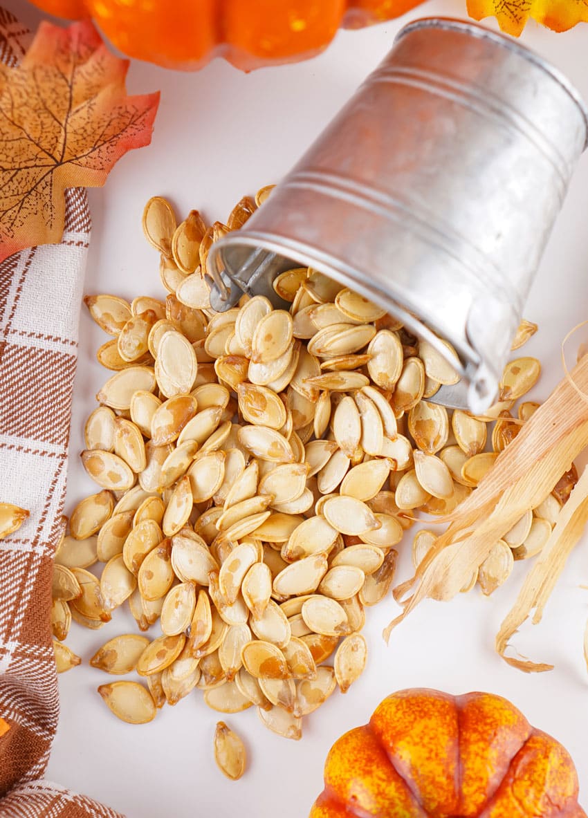 homemade roasted pumpkin seeds spilling out of a small metal pail onto a white countertop