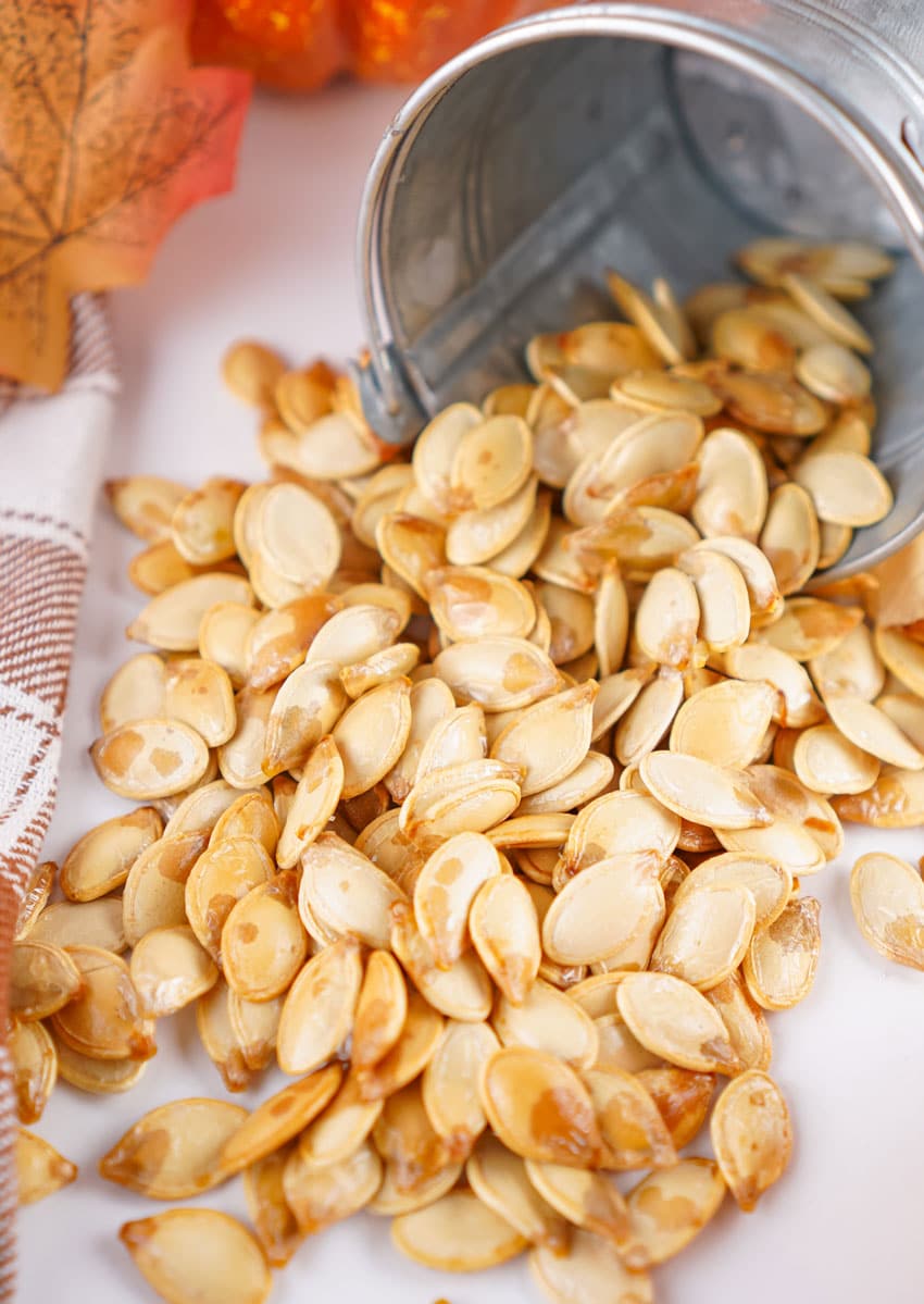 homemade roasted pumpkin seeds spilling out of a small metal pail onto a white countertop