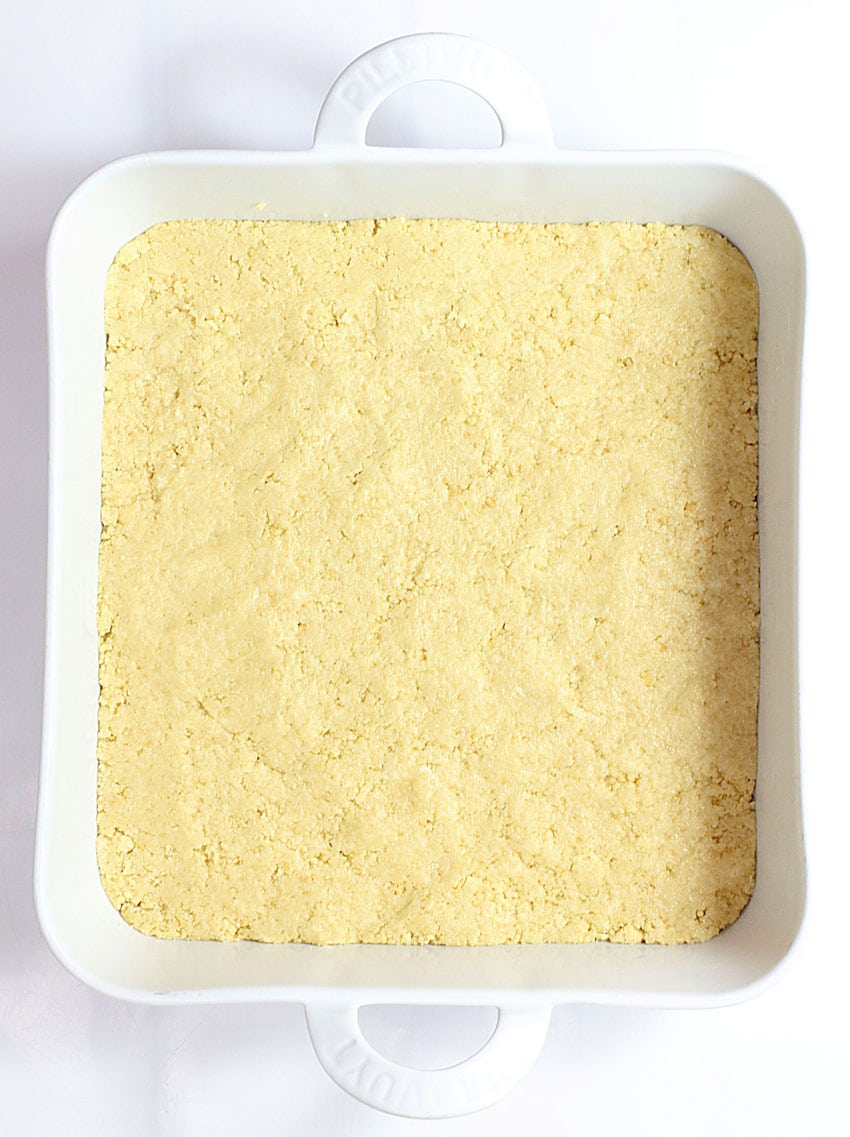 a graham cracker crust pressed evenly out in the bottom of a white square baking dish