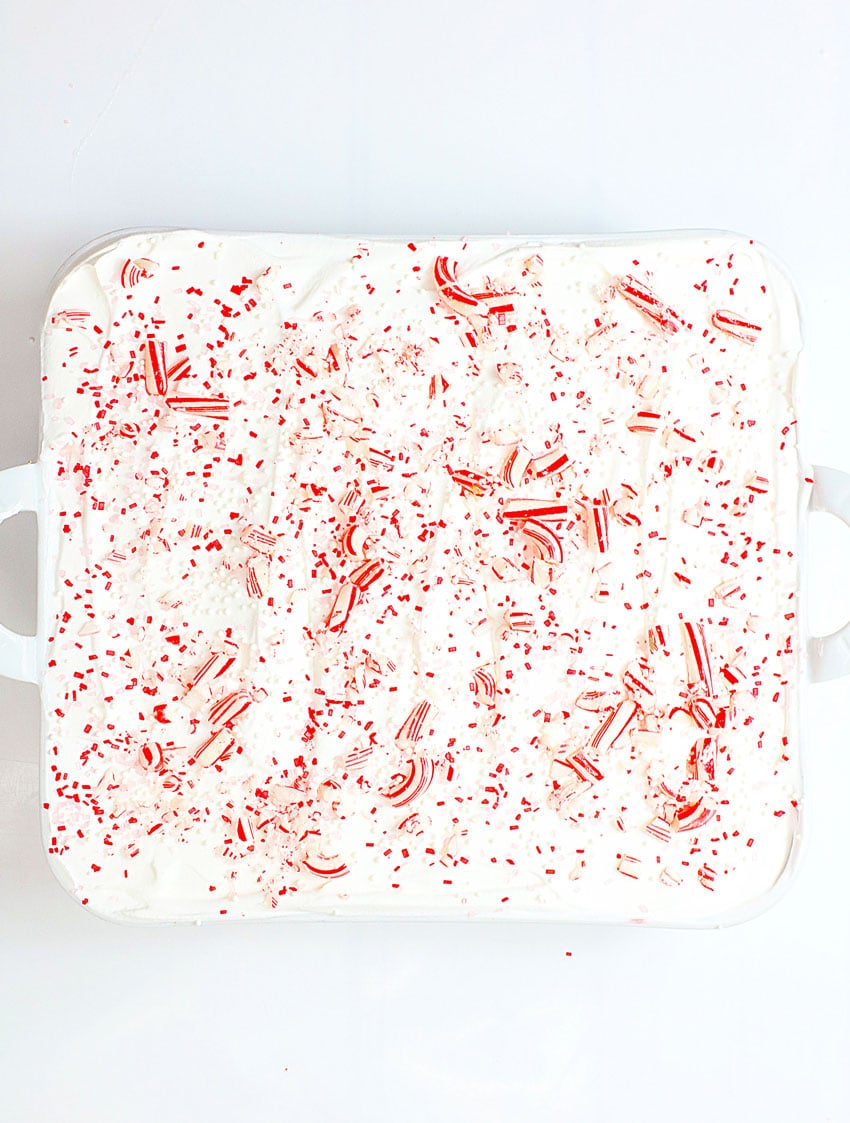 an overhead image showing a candy cane lush dessert topped with peppermint candy pieces in a white square baking dish