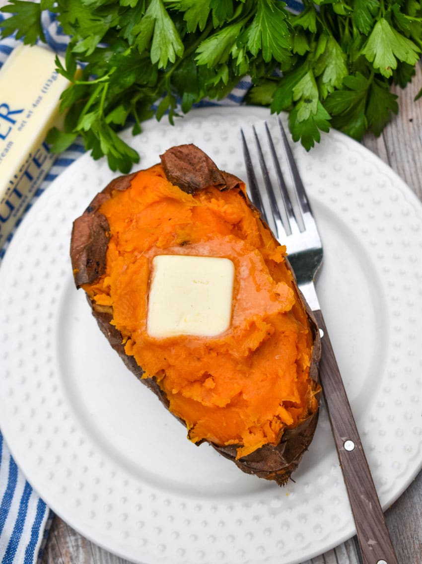 an air fryer baked sweet potato topped with a melting pat of butter on a small white plate with a fork resting on the side