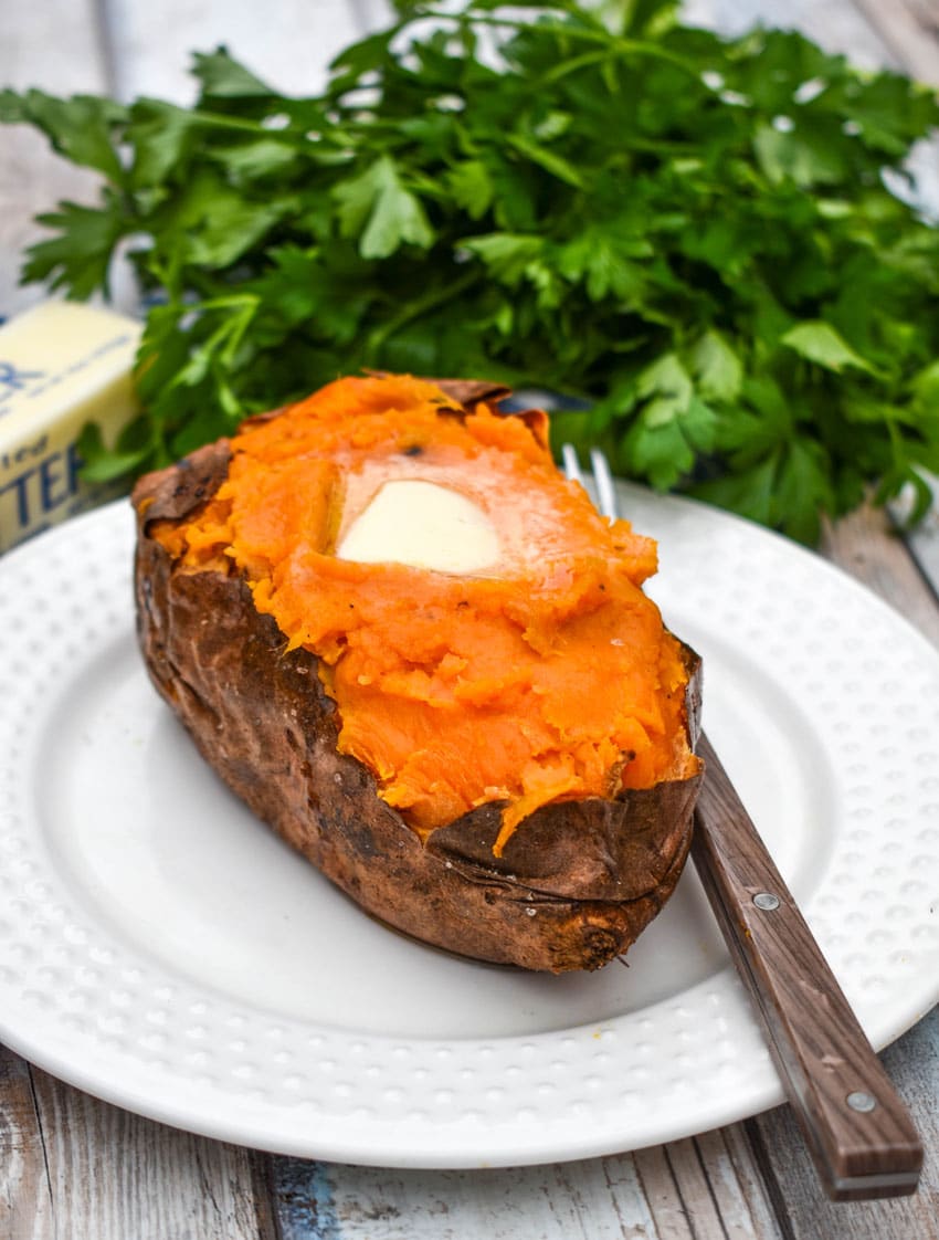 an air fryer baked sweet potato topped with a melting pat of butter on a small white plate with a fork resting on the side